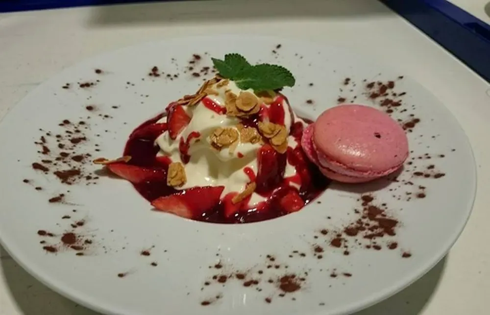 Dessert gourmand avec crème, fraises, amandes et macaron rose.